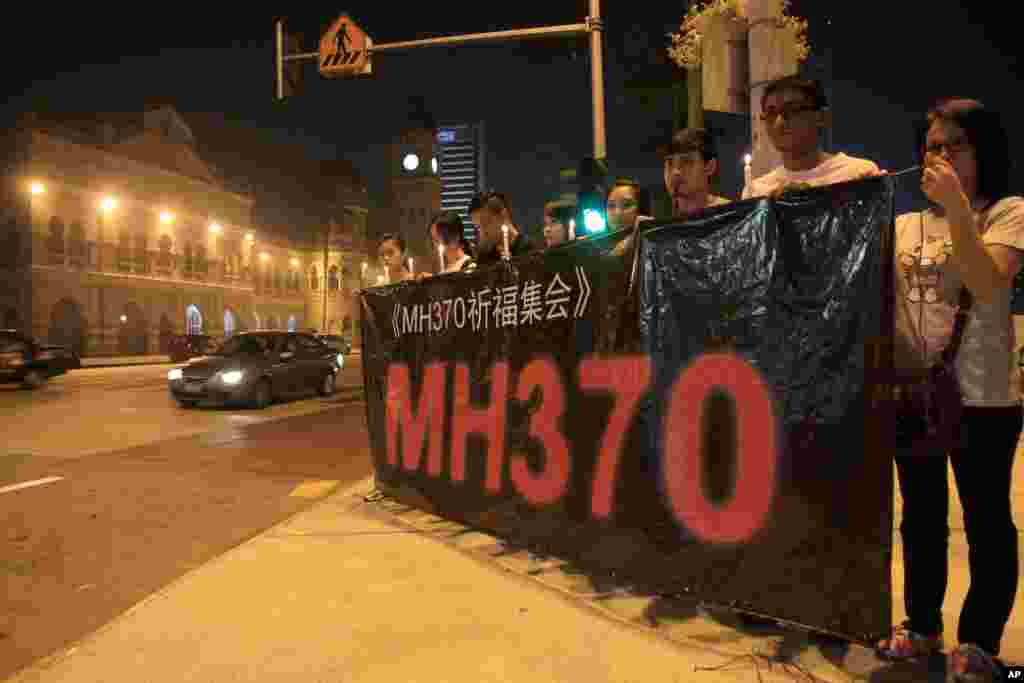 People hold a banner and candles during a candlelight vigil for passengers aboard a missing Malaysia Airlines plane in Kuala Lumpur, Malaysia, March 10, 2014. 