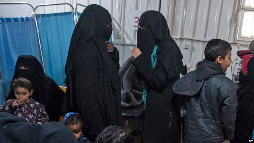 Two women (C), reportedly wives of Islamic State (IS) group fighters, wait with other women and children at a makeshift clinic at the Internally Displaced Persons (IDP) camp of al-Hol in al-Hasakeh governorate in northeastern Syria, Feb. 7, 2019. 