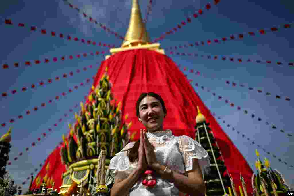 A woman poses in front of the Phra Borom Banphot Chedi, or stupa, draped in red cloth atop the Wat Saket Buddhist temple in Bangkok on Nov. 8, 2024, to mark the start of a 10-day annual fair ahead of Thailand's Loy Krathong festival.