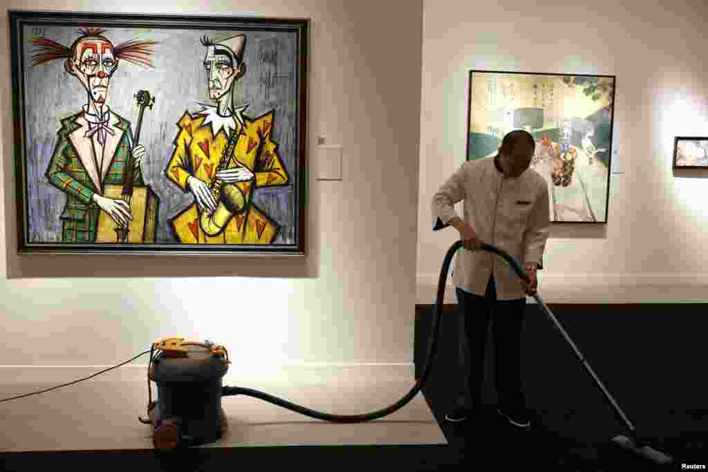 An employee vacuums the carpet next to Bernard Buffet's "Deux clowns, saxophone" during a media preview of Christie's Shanghai Spring Auction in China. Christie's will present the auction on April 26.