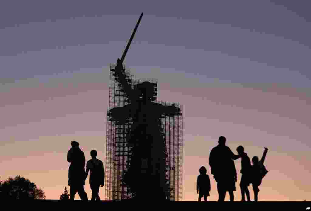 People walk near the statue 'The Motherland Calls' under reconstruction in Mamayev Kurgan, the main place of the Battle of Stalingrad memorial, during sunset in Volgograd, Russia, Aug. 12, 2019.