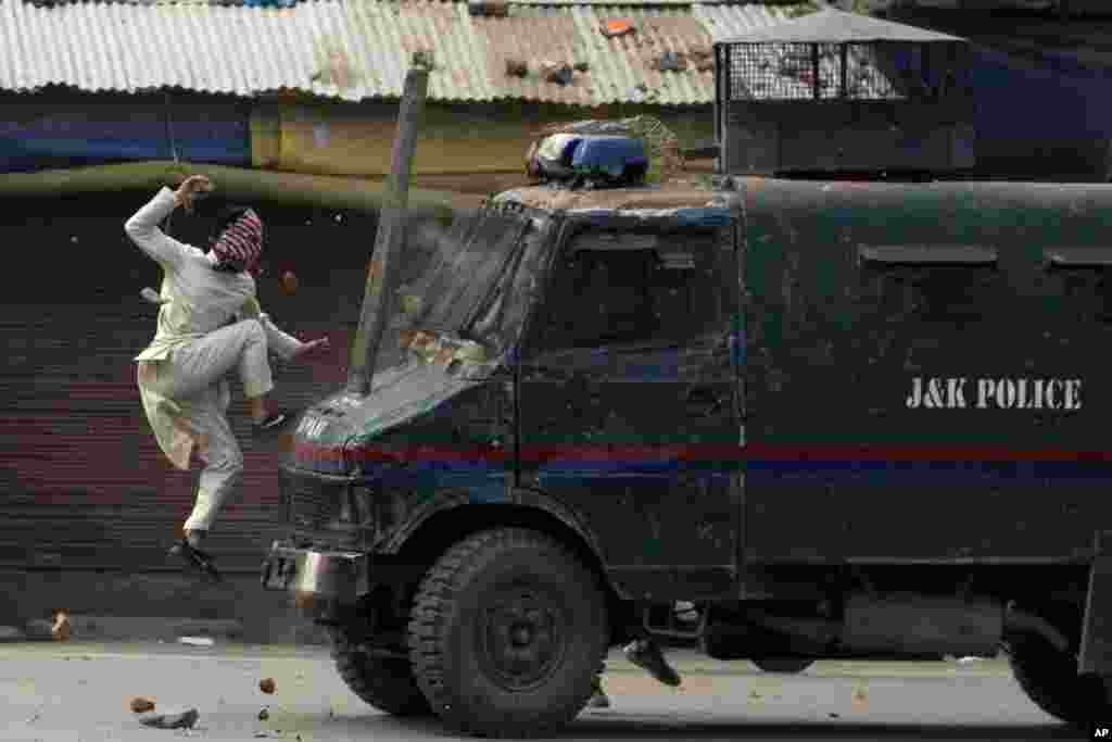 A masked Kashmiri protester jumps on the bonnet of an armored vehicle of Indian police as he throws stones at it during a protest in Srinagar, Indian-controlled Kashmir.