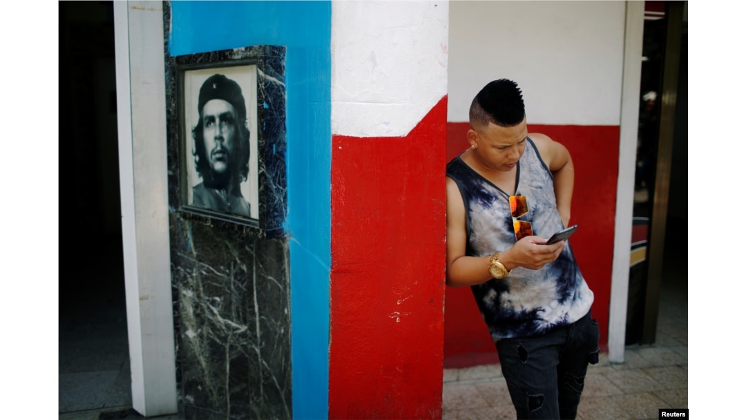 A young Cuban checks his phone at an internet hotspot next to a picture of late revolutionary hero Ernesto "Che" Guevara in Havana, Aug. 10, 2018.
