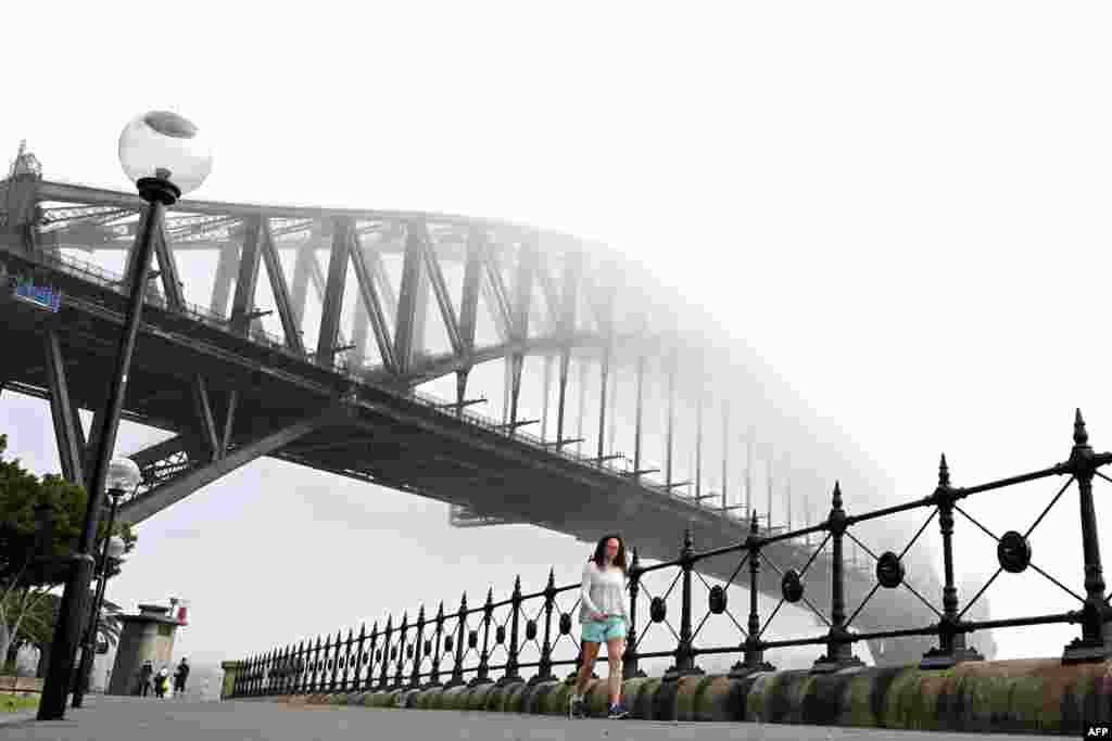 People walk under Australia's iconic landmark Harbour Bridge in Sydney, Australia, as heavy fog blankets the city.