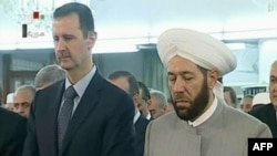 An image grab taken from the state-run Syrian television on August 8, 2013, shows Syrian President Bashar al-Assad (L) and Syrian Grand Mufti Ahmed Hassun attending the morning prayer of Eid al-Fitr in Damascus.