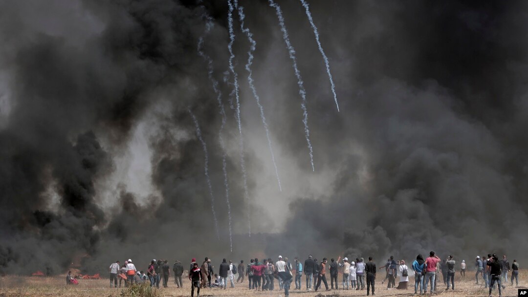 Palestinian protesters gather in front of burned tires while Israeli soldiers fire teargas during clashes with Israeli troops along Gaza's border with Israel, east of Khan Younis, Gaza Strip, Friday, April 6, 2018.