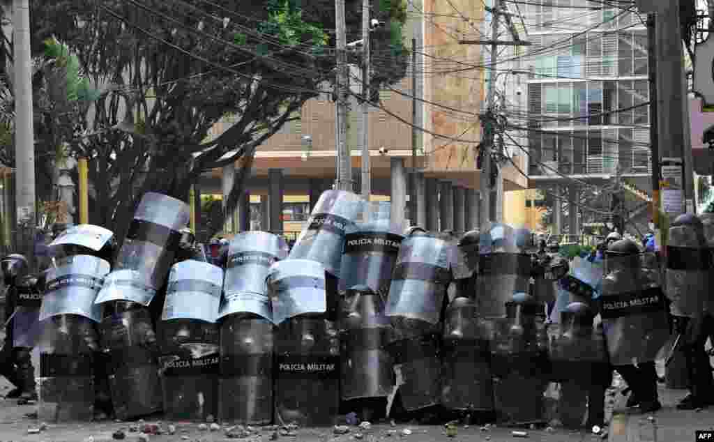 Honduran riot police take cover during clashes with students of the National Autonomous University of Honduras (UNAH) and elementary school teachers who protest against the approval of education and healthcare bills in the Honduran Congress in Tegucigalpa, April 29, 2019.