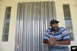 In this Jan. 9, 2018 photo, retiree Ramon Santiago sits on his front porch, less than a block away from where three bodies were discovered near a basketball court, in Carolina, Puerto Rico.
