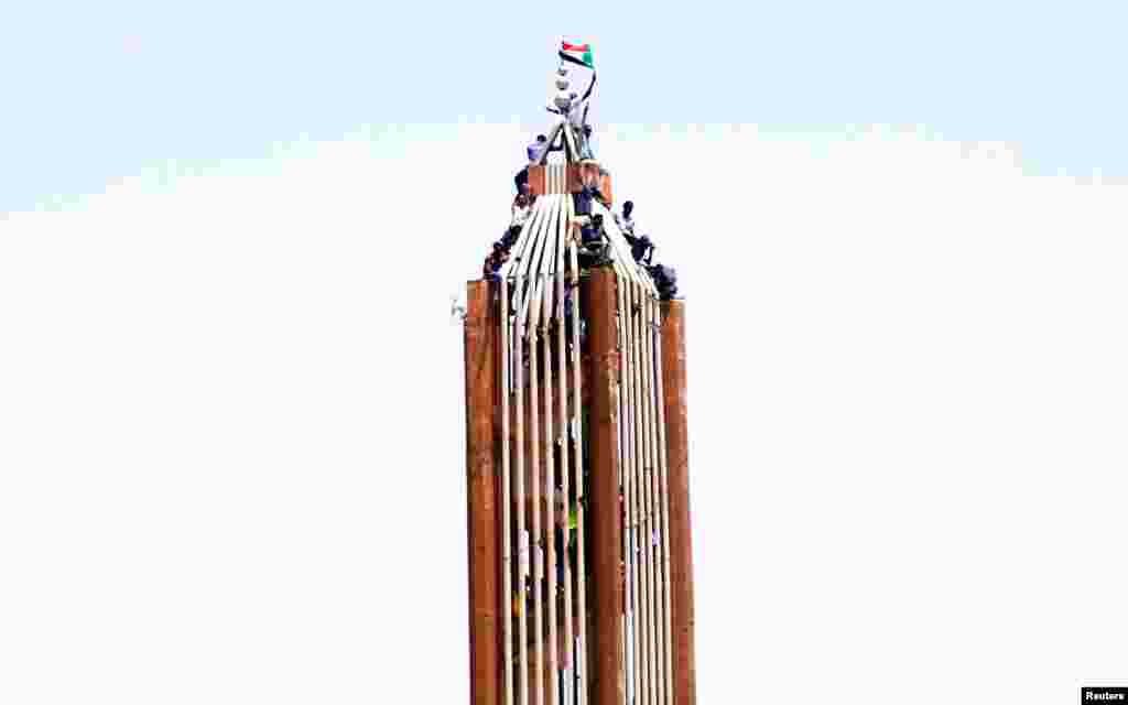 Sudanese demonstrators hold their national flag on top of a building in Khartoum after the country's Defense Minister Awad Mohamed Ahmed Ibn Auf said that President Omar al-Bashir had been detained "in a safe place" and that a military council would run the country for a two-year transitional period.