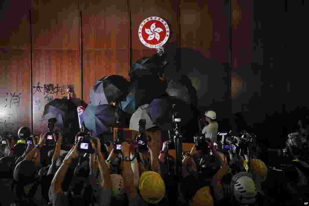 Journalists film a protester defaces the Hong Kong emblem inside the meeting hall of the Legislative Council in Hong Kong. Protesters took over the legislature's main building, tearing down portraits of legislative leaders and spray painting pro-democracy slogans on the walls of the main chamber.