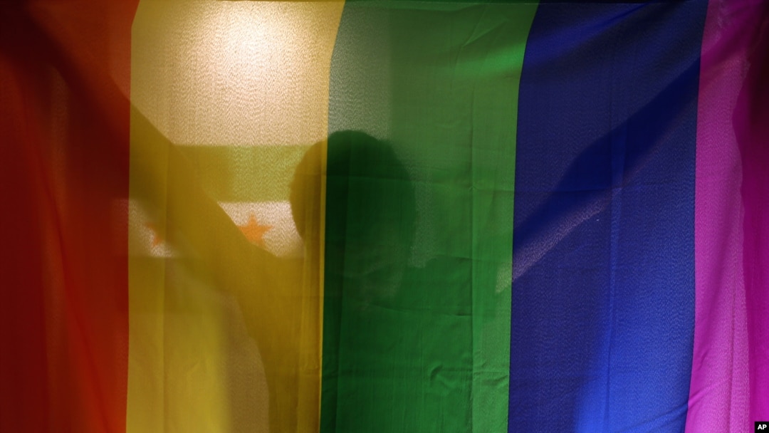 FILE - A person poses with the rainbow flag symbolic of LGBT rights. A TV host in Egypt has been sentenced to prison for interviewing a gay sex worker on his show in August 2018.