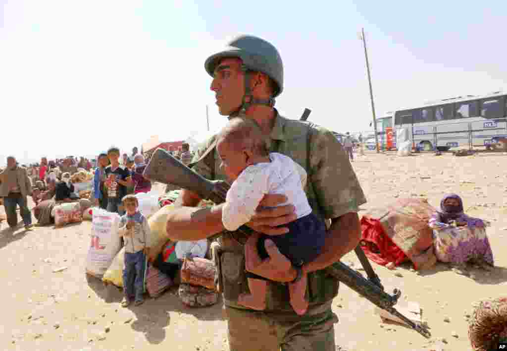A Turkish soldier holds a lost baby as he looks for its mother, as thousands of new Syrian refugees from Kobani arrive at the Turkey-Syria border crossing of Yumurtalik near Suruc, Turkey, Oct. 2, 2014.