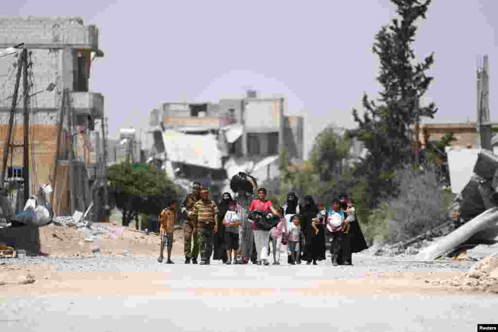 Syria Democratic Forces (SDF) fighters walk with people whot fled their homes due to clashes between Islamic State fighters and SDF in Manbij, in Aleppo Governorate.