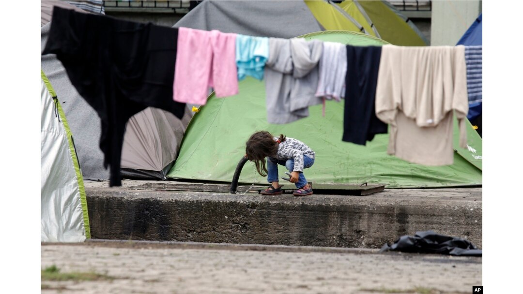 FILE - A child drinks water from a pipe on the platform of a train station which was turned into a makeshift camp crowded by migrants and refugees at the northern Greek border point of Idomeni, Greece, May 2, 2016.
