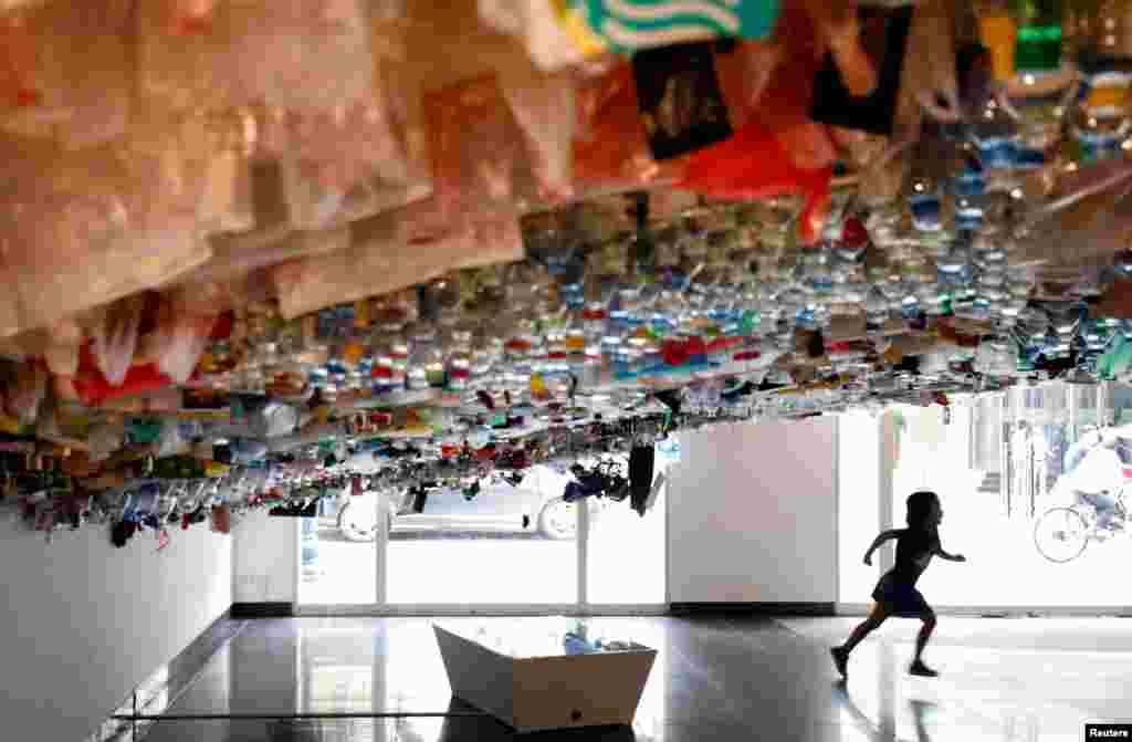 A girl runs during an exhibition of a hanging art installation made from scraps of plastic bags, bottles, cans and containers, entitled 'Reduce', at the French Cultural Center in Hanoi, Vietnam.