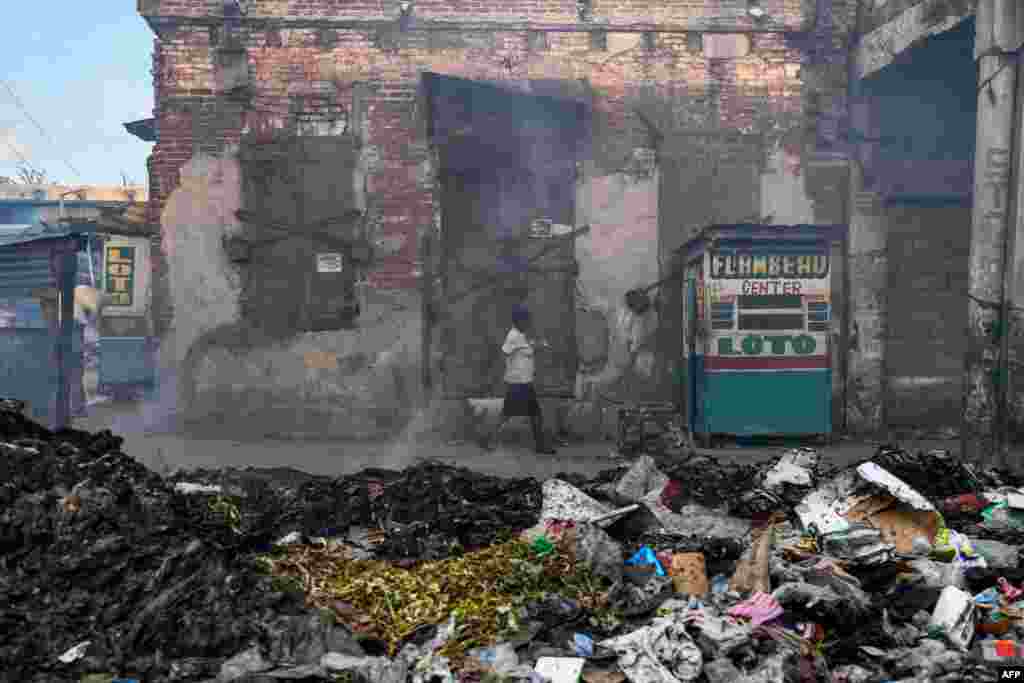 A woman walks past a burning garbage dump in Port-au-Prince, Haiti, Aug. 5, 2019.