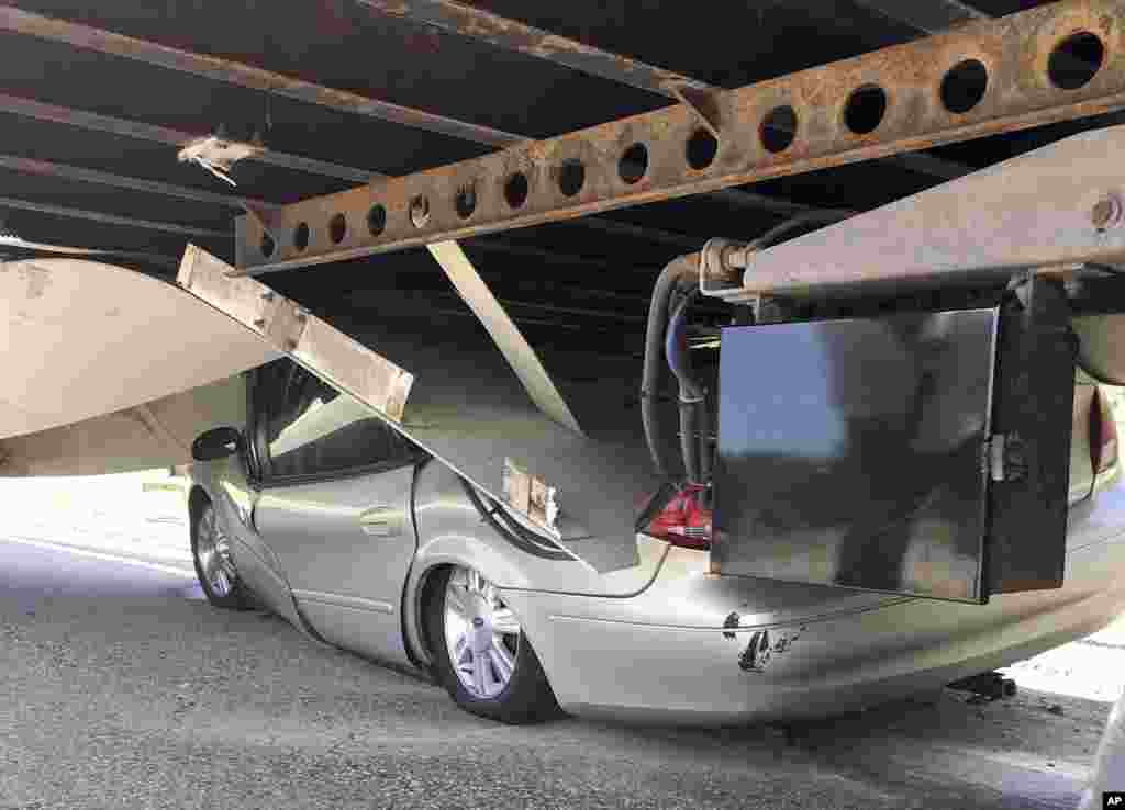 In this photo released by the Uxbridge Fire Department on its Facebook page, a car sits wedged under a tractor-trailer on Route 146 in Uxbridge, Massachusetts. The motorist, whose name wasn't made public, climbed out of the driver's side door of the crushed car and wasn't seriously hurt.