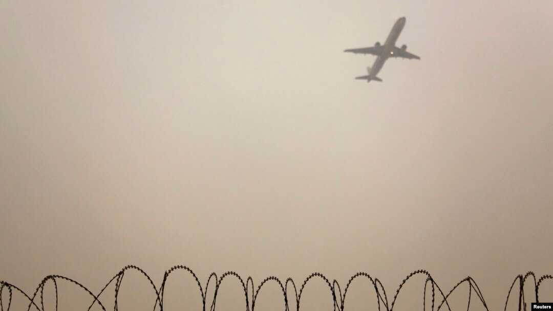 FILE - A plane flies in the polluted air above the airport fences in Beijing, Feb. 22, 2012.