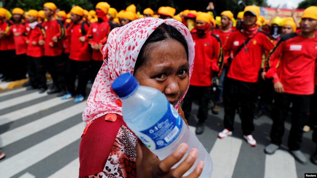 FILE - A street vendor holds drinking water as she walks near workers attending a May Day rally in front of presidential palace in Jakarta, Indonesia, May 1, 2016. 