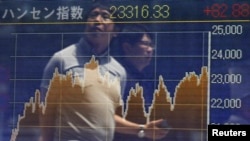 FILE - Passersby are reflected on in electronic graph showing recent movements of the Hang Seng Index outside a brokerage in Tokyo.