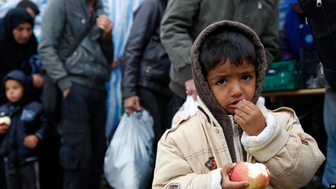 A child eats an apple waiting in line to cross the Serbian-Croatian border, at the village of Berkasovo, near Sid, Serbia, Oct.15, 2015.
