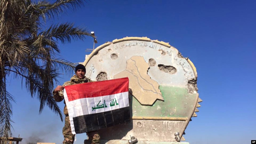 Un soldado iraquí sostiene la bandera nacional en el complejo de gobierno en Ramadi, al occidente de Bagdad. Dic. 28 de 2015.