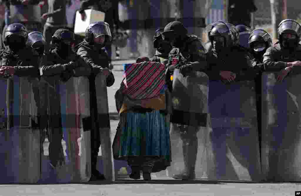 Police make way for an elderly woman to pass through as they guard the new coca leaf market on the third day of clashes with coca farmers in La Paz, Bolivia, Aug. 3, 2022.