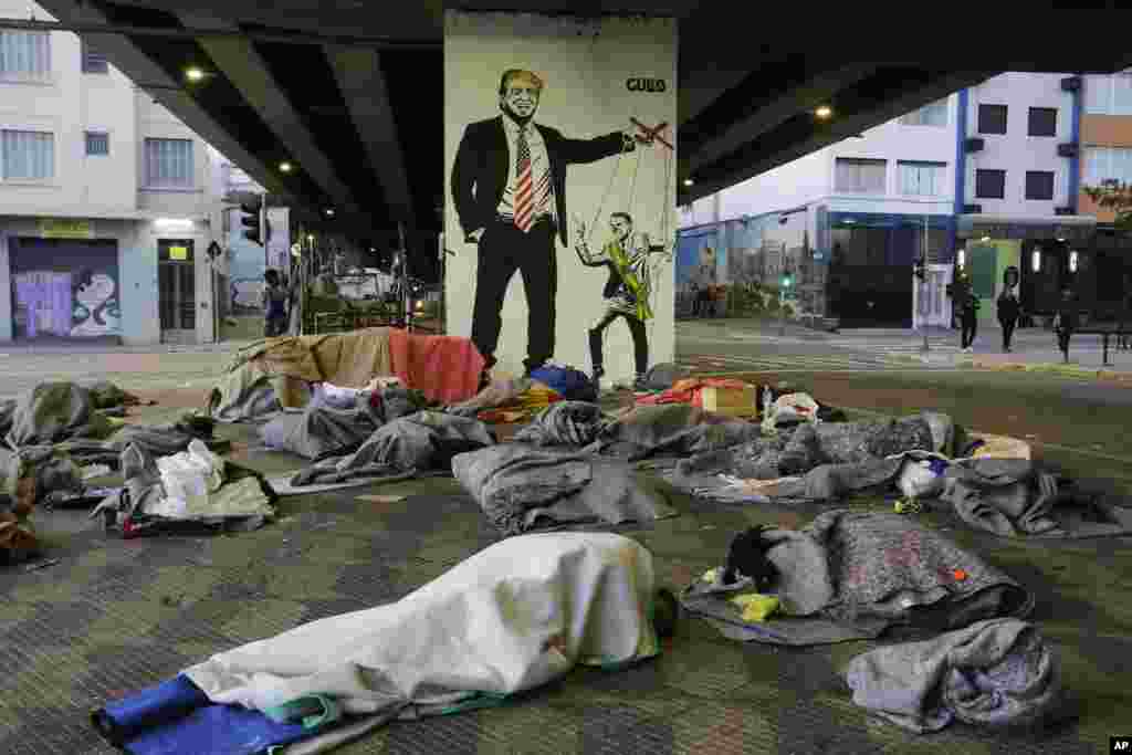 Homeless people sleep under a bridge in front of a mural depicting US President Donald Trump as a puppeteer manipulating Brazil's President Jair Bolsonaro, in downtown Sao Paulo, Brazil.