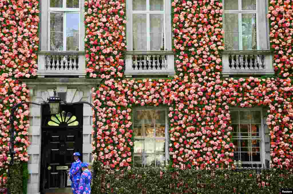 Doormen dressed in floral patterned suits stand on duty outside of a private club with it's front covered in flowers in London.
