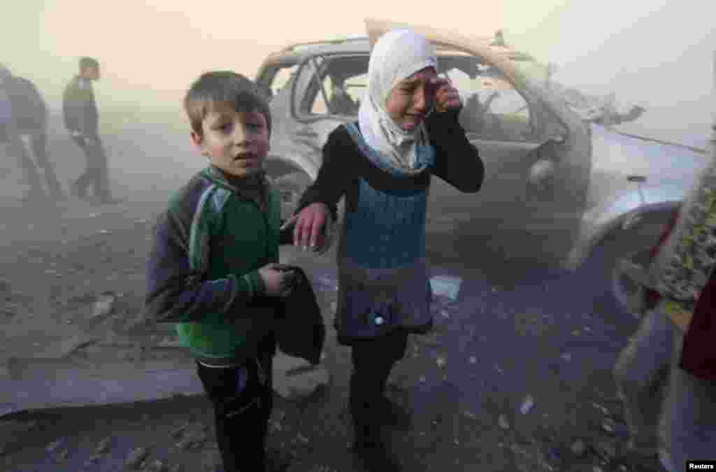 A girl and boy are shaken as they stand near a site hit by what activists said were barrel bombs dropped by government forces in Aleppo, Syria, Jan. 29, 2014. 
