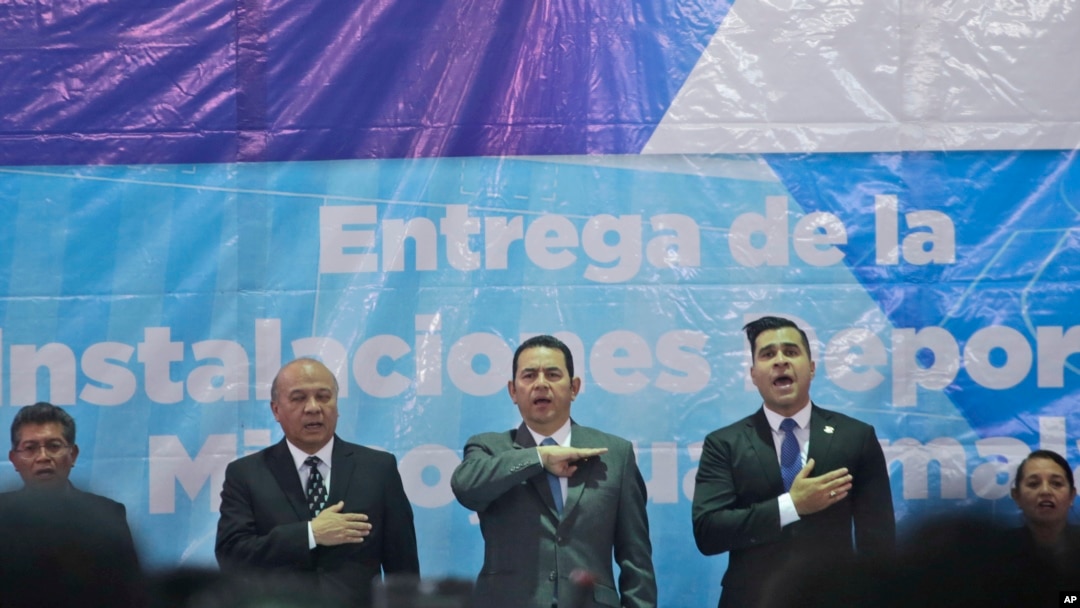 El presidente guatemalteco, Jimmy Morales, al centro, canta el himno nacional acompañado del alcalde de Mixco, Ernesto Bran, a la derecha, y el ministro de cultura, Jose Chex, durante la inauguración de un campo de fútbol en Mixco, Guatemala, el 17 de septiembre del 2018. 