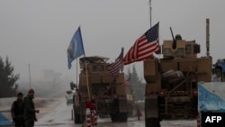 FILE - A line of U.S. military vehicles drive through a checkpoint of the Internal Security Forces in Manbij as they head to their base on the outskirts of the northern Syrian city, Dec. 30, 2018.