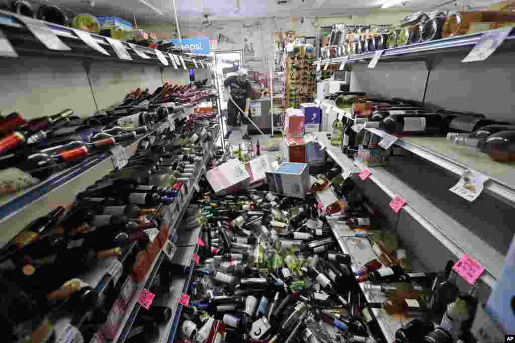 Bottles of wine are strewn in the middle of an aisle as Victor Abdullatif, background center, mops inside of the Eastridge Market, his family's store, July 6, 2019, in Ridgecrest, California. Crews in Southern California assessed damage to cracked and burned buildings, broken roads, leaking water and gas lines and other infrastructure after the largest earthquake the region has seen in nearly 20 years jolted an area from Sacramento to Las Vegas to Mexico.