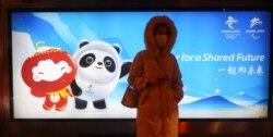 A woman waits on a bus station in front of an advertising board featuring Bing Dwen Dwen, the Beijing 2022 Winter Olympic Mascot and Shuey Rhon Rhon, the 2022 Beijing Winter Paralympic Games Mascot, in Beijing on January 19, 2022. (Fabrizio Bensch/Reuters)