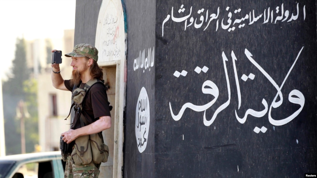 FILE - A militant Islamist fighter uses a mobile device to film his fellow fighters taking part in a military parade along the streets of Syria's northern Raqqa province.