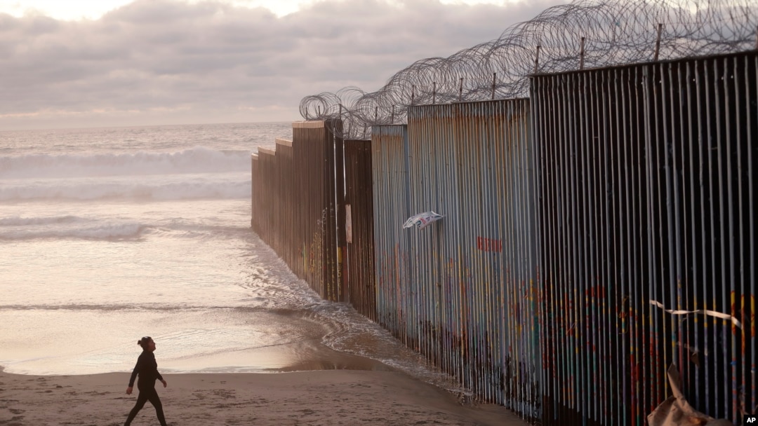 A woman walks on the beach, Jan. 9, 2019, next to the border wall topped with razor wire in Tijuana, Mexico.