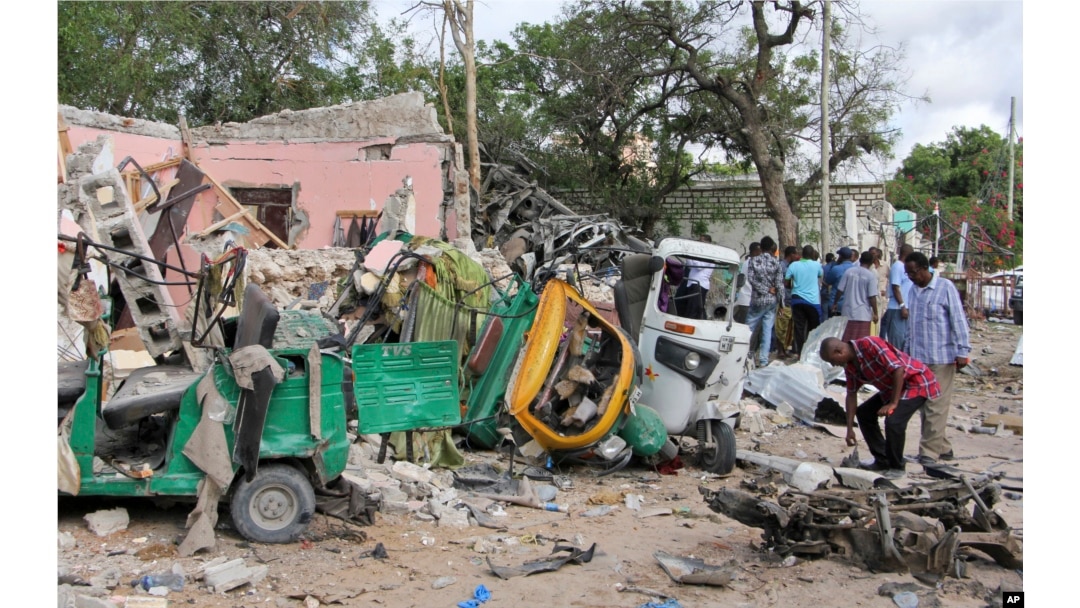 FILE - Somalis walk near destroyed vehicles at the scene of a car bomb blast and gun battle targeting a restaurant in Mogadishu, June 15, 2017.