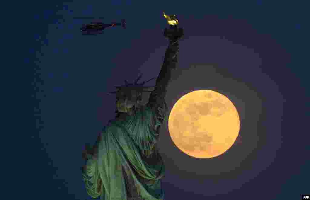 A helicopter flies past as the full moon rises behind the Statue of Liberty in New York City, May 18, 2019.