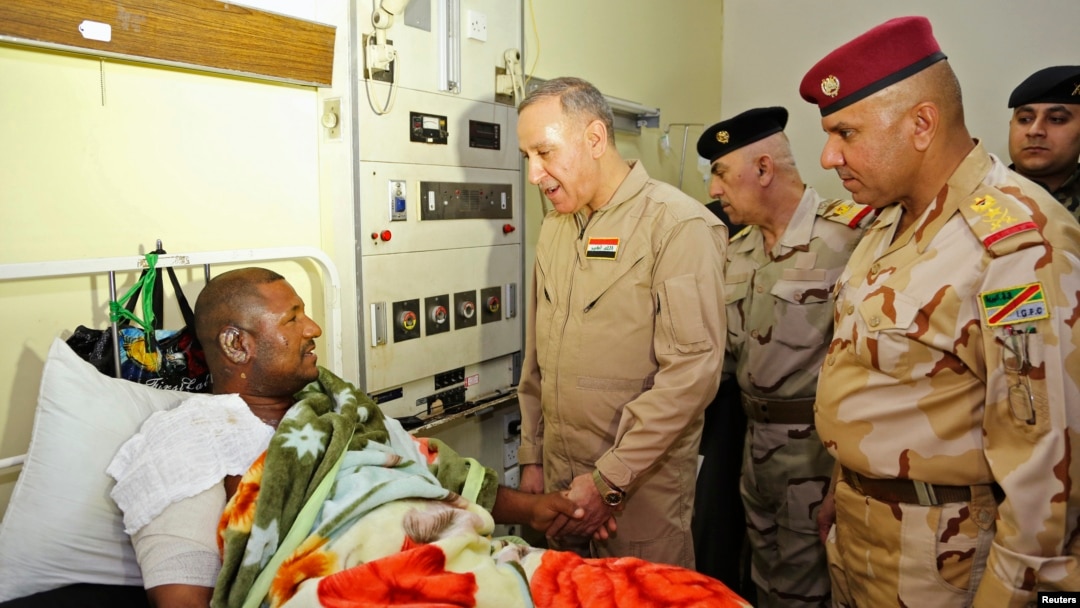 Iraqi Defense Minister Khaled al-Obeidi talks to a soldier wounded in the battle for Baiji during a hospital visit in Baghdad, Nov. 15, 2014. 