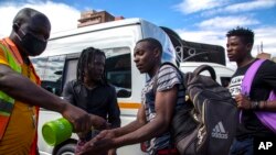 Jacob Maphala, un regulador de taxis con una máscara facial, rocía desinfectante a los pasajeros para protegerse contra el coronavirus, en una estación de taxis en Johannesburgo, Sudáfrica. Marzo 26 de 2020.