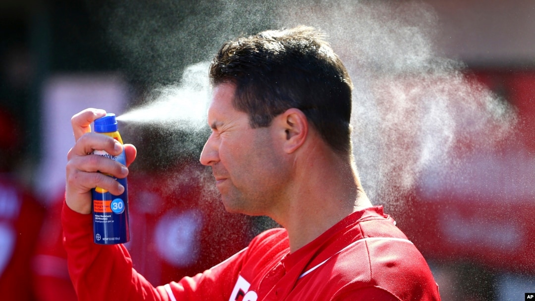 FILE - Cincinnati Reds third base/catching coach J.R. House applies sunscreen to his face while in the dugout during the third inning of a spring training baseball game against the Cleveland Indians Saturday, Feb. 23, 2019, in Goodyear, Ariz. (AP Photo/Ro