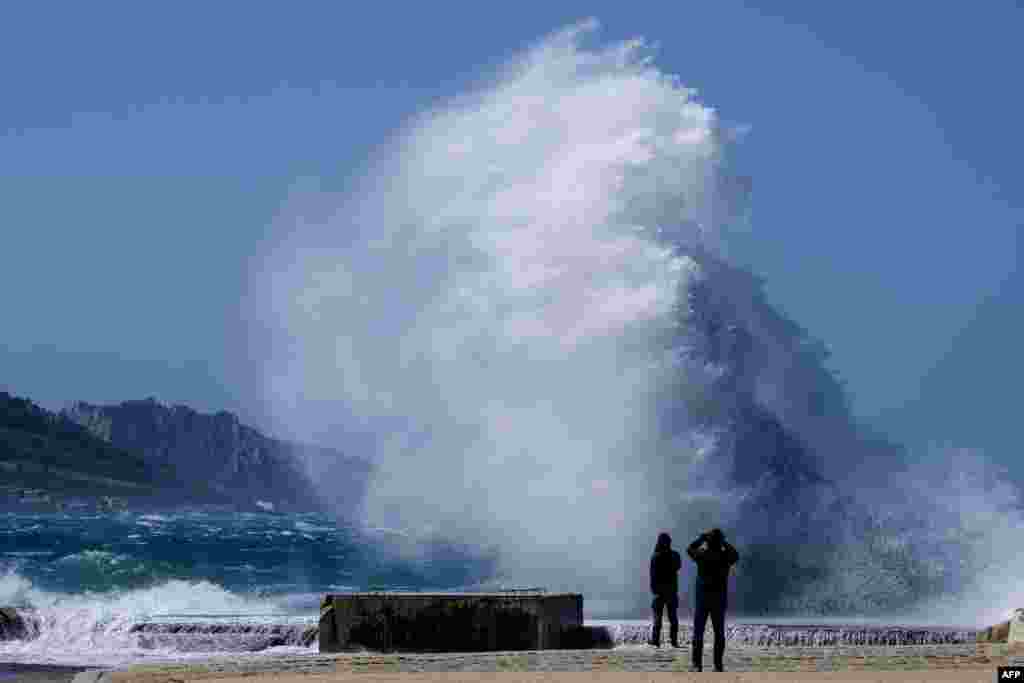 People watch heavy waves hiting the shore at the Plage du David beach in downtown Marseille, as storm Eleanor hits southern parts of France.