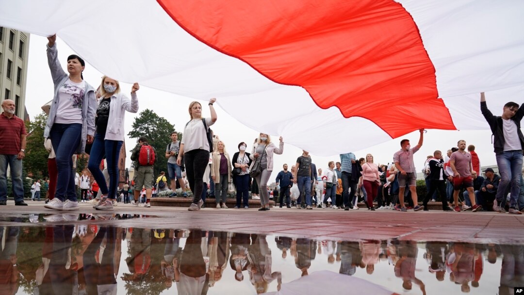 Belarusian opposition supporters carry a huge old Belarusian national flag as rally toward Independence Square in Minsk, Belarus, Aug. 23, 2020. 