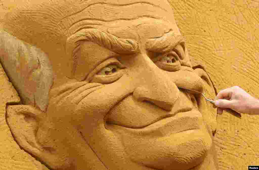 A sand carver works on a sculpture depicting French actor Louis de Funes, during the Sand Sculpture Festival "Dreams" in Ostend, Belgium.