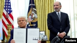 Президент США Дональд Трамп держит в руках указ о повышении тарифов. Рядом с ним в Овальном кабинете Белого дома министр торговли США Говард Латник. 13 февраля 2025 года. REUTERS.