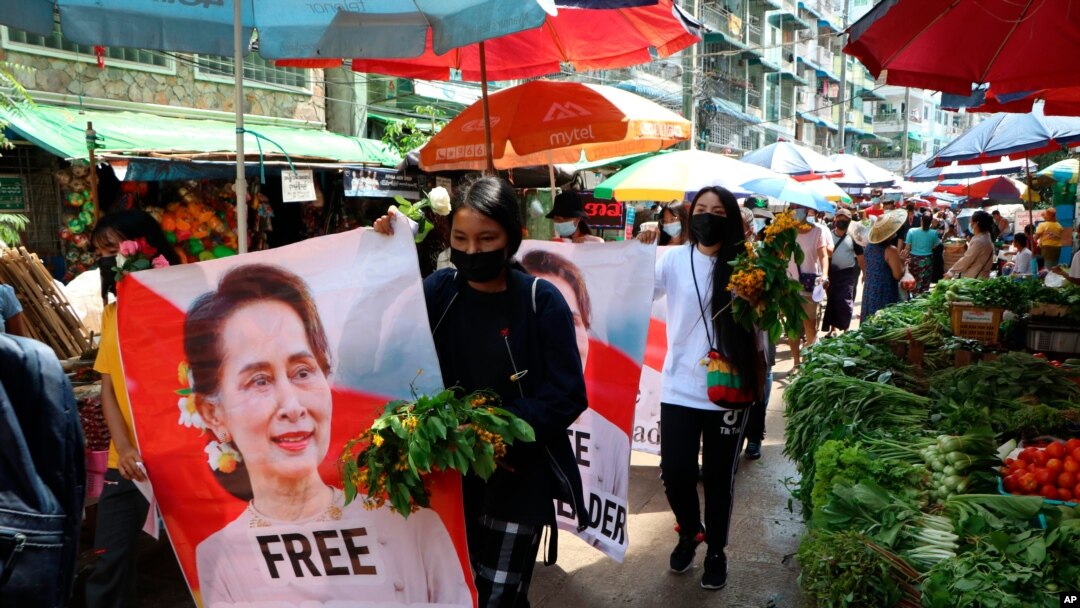 Waandamanji wakipinga mapinduzi wakipita sokoni na picha za kiongoz aliyepinduliwa Aung San Suu Kyi katika mji wa Kamayut, Yangon, Myanmar Alhamisi, April 8, 2021. 