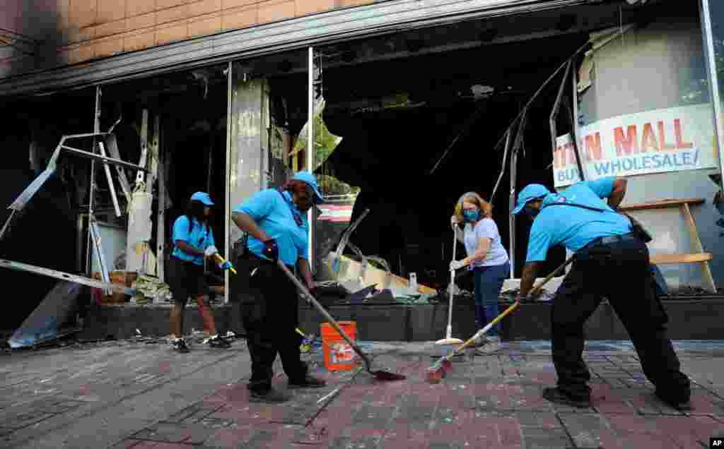 Workers and a volunteer clean up damage outside a burned-out clothing store in Birmingham, Alabama, June 1, 2020, following a night of unrest.