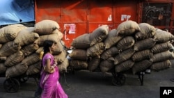 An Indian woman walk past carts loaded with sacks of food items at a wholesale market in New Delhi, India, June 9, 2011.