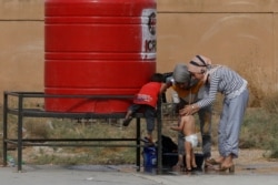 FILE - A displaced Syrian Kurdish woman, who fled violence with her family after a Turkish offensive in northeastern Syria, gives one of her children a shower at a public school they use as a temporary shelter, in Hasakah, Syria, Oct. 22, 2019.