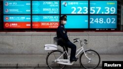 一名戴著口罩的日本警察騎車停站在東京街頭一個日經指數電子顯示板前。 （2020年2月26日）